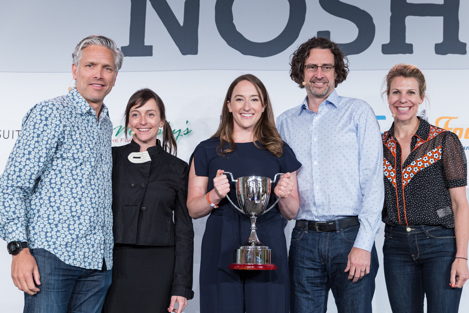 Four Pitch Slam judges and the winning team posing together with the trophy on stage