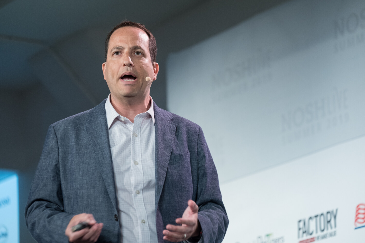 Speaker in a blue-gray textured blazer and white shirt speaking with open hands