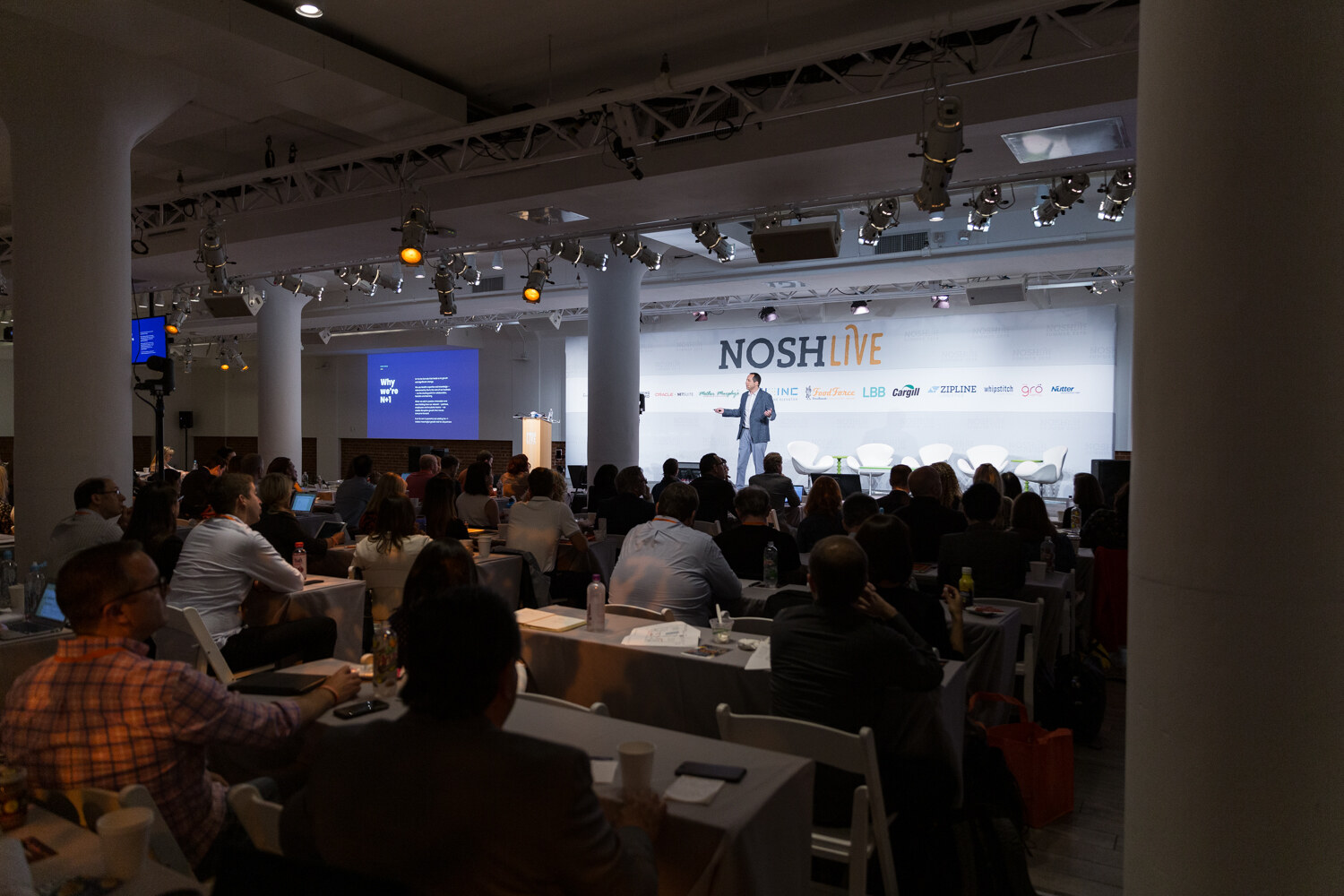 Wide view of the main hall with the speaker on stage and a slide on the screen