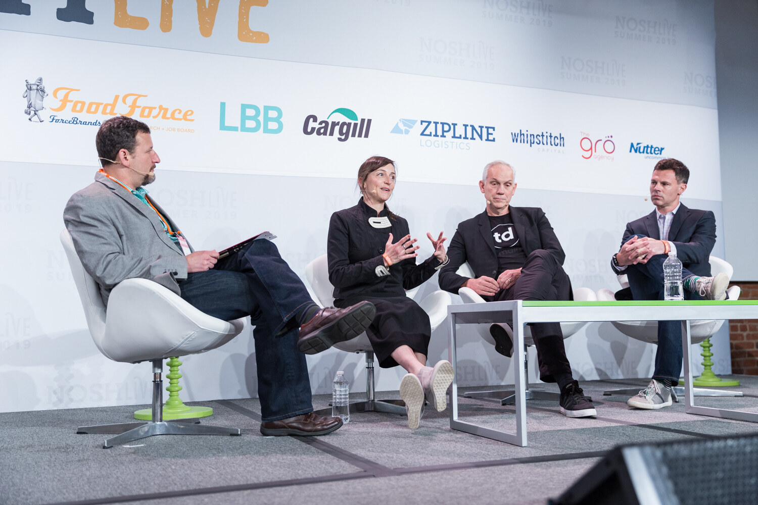 Moderator in a gray blazer with a woman in a black jacket, a man in a black td T-shirt and a man in a navy blazer seated on stage during the Brokers session