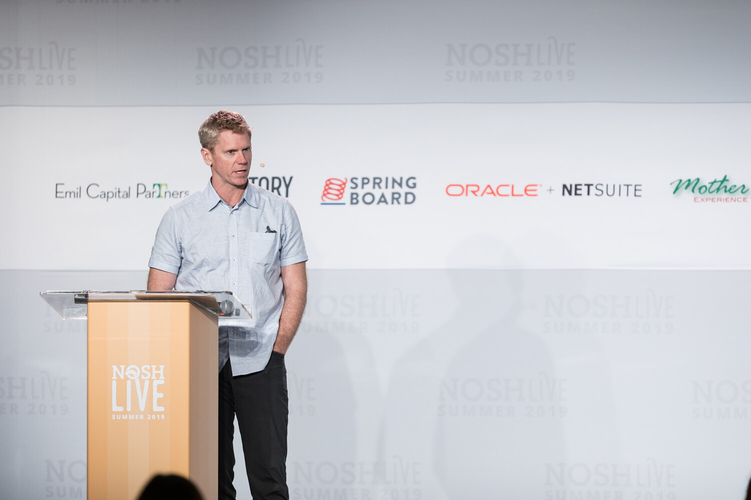 Speaker in a light blue short-sleeve shirt standing at the NOSH LIVE lectern