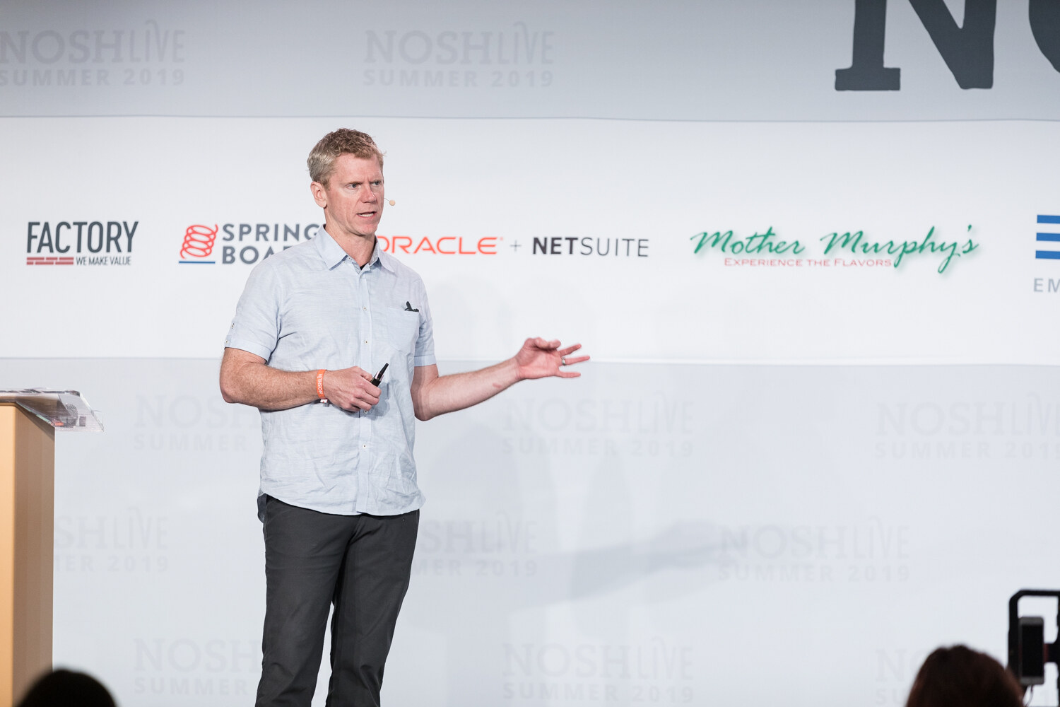 Speaker in a light blue shirt gesturing in front of the sponsor wall