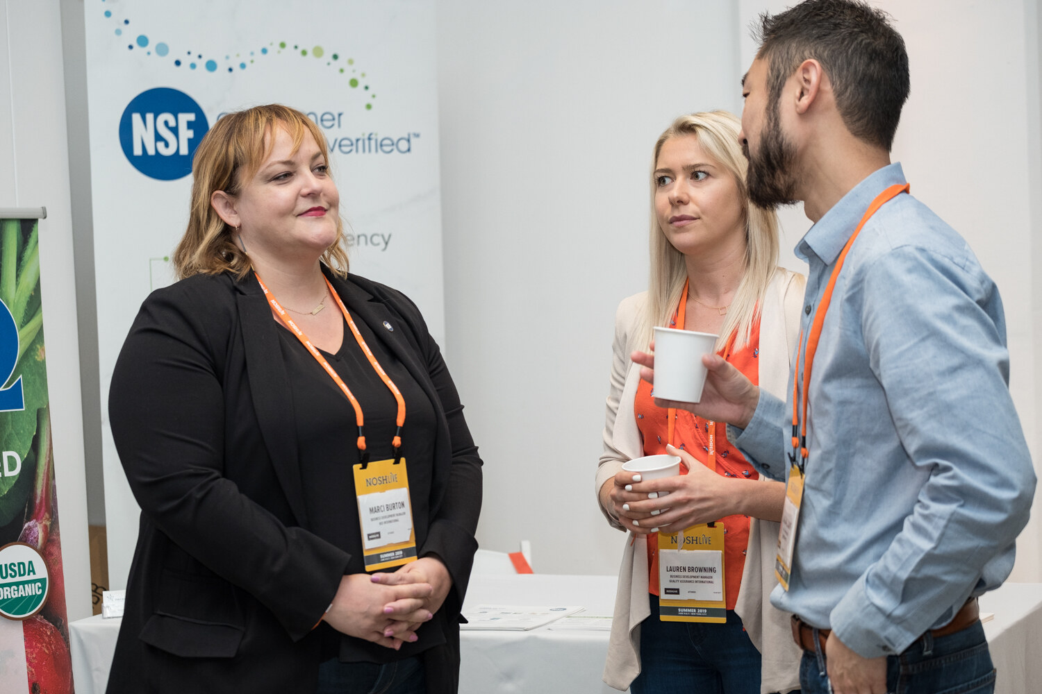 Woman in a black blazer, a blond woman and a man talking at an NSF consumer values verified booth
