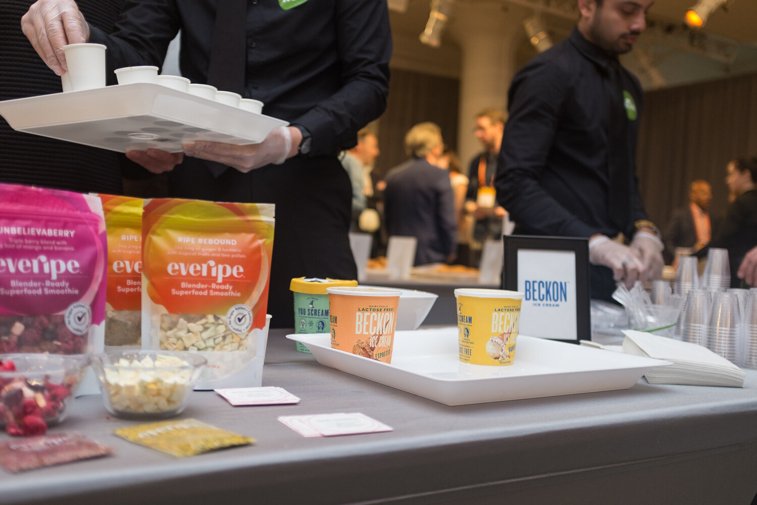 Server with a tray of sample cups beside everipe pouches and a Beckon sign