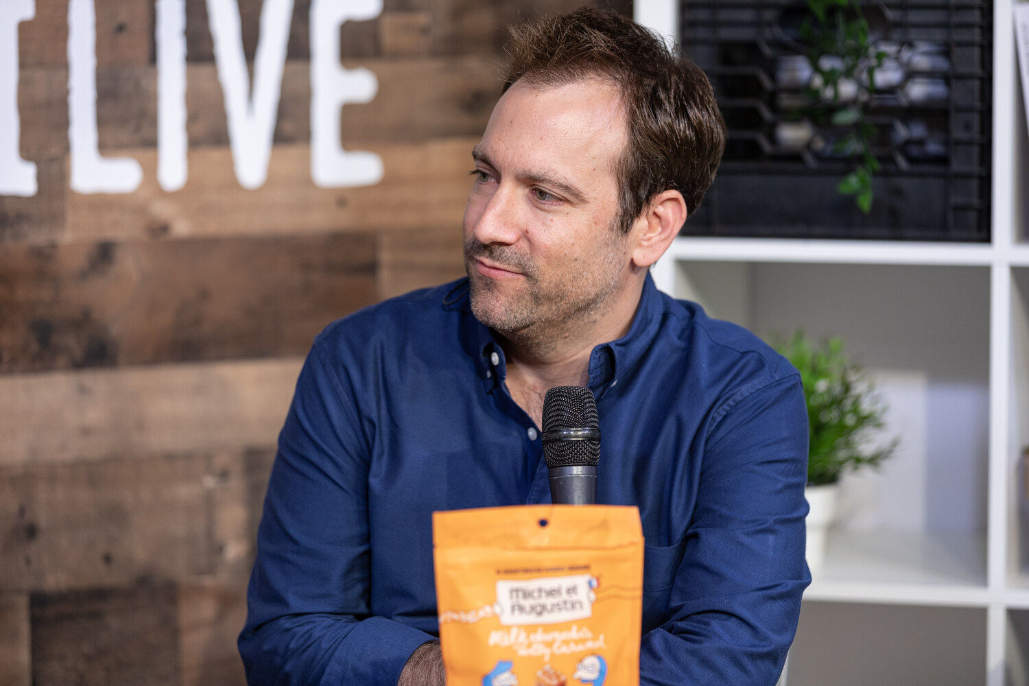 Man in a navy button-up shirt looking aside behind a bag of Michel et Augustin snacks