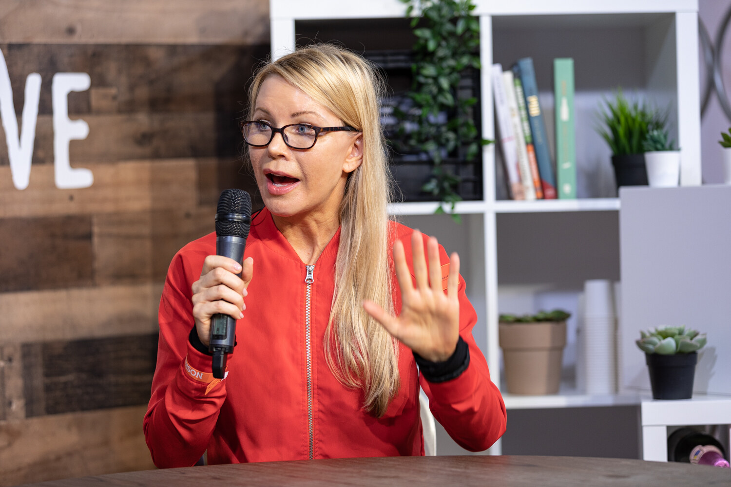 Woman in a red zip jacket with her palm raised, mid-story