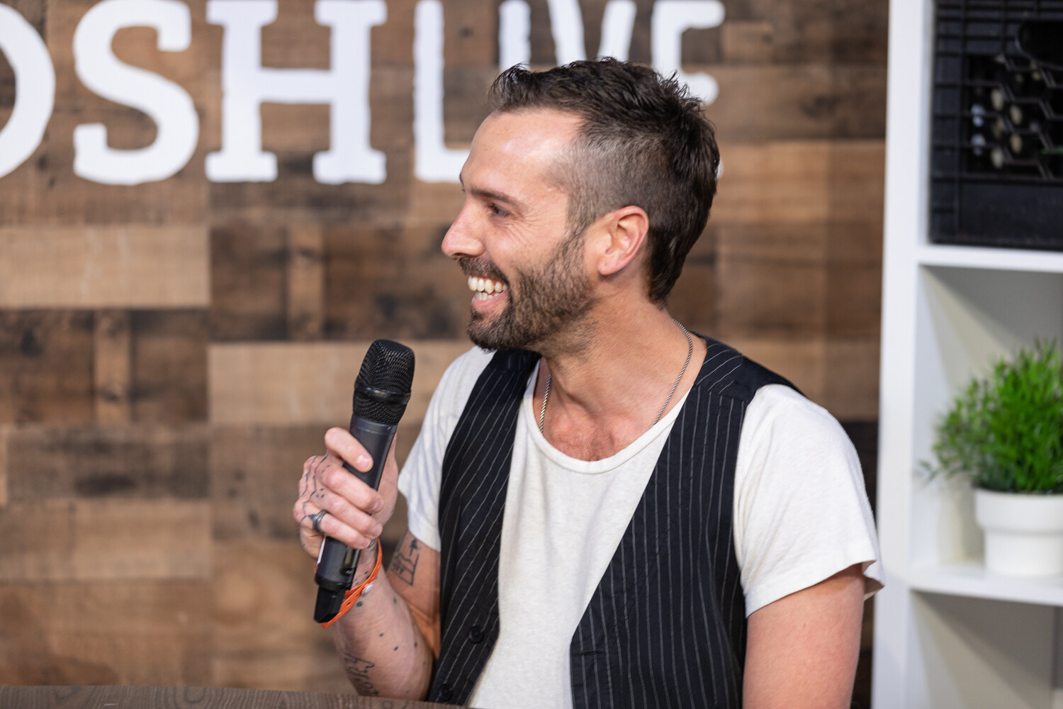 Man in a pinstriped vest laughing while holding a microphone
