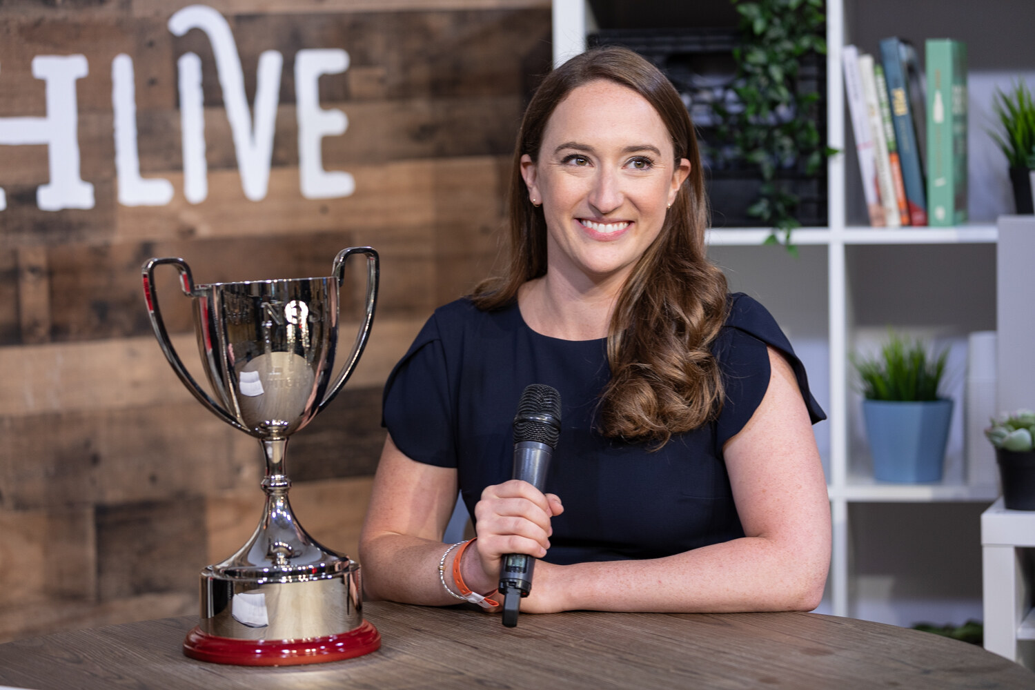 Pitch Slam winner in a navy dress smiling beside the trophy at the Taste Radio livestream table in front of a NOSHLIVE wooden wall