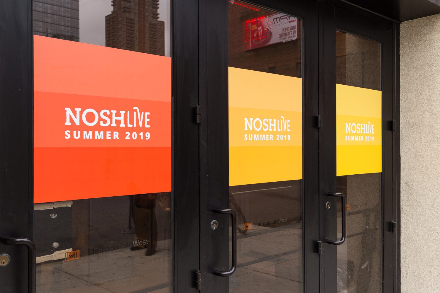 Entrance doors with orange and yellow NOSHLIVE Summer 2019 window graphics