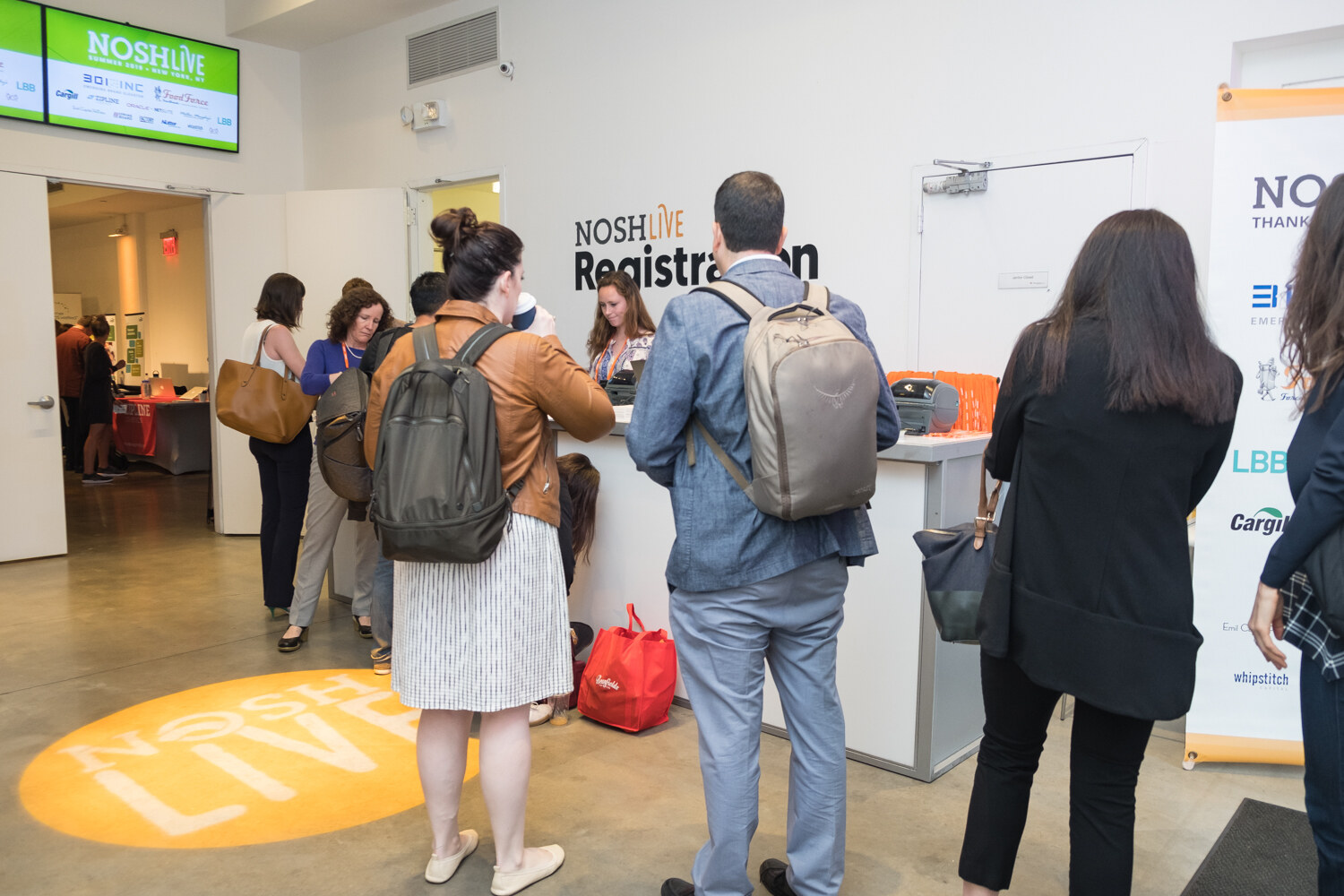 Wide view of the registration area with attendees in line and a NOSH LIVE light on the floor