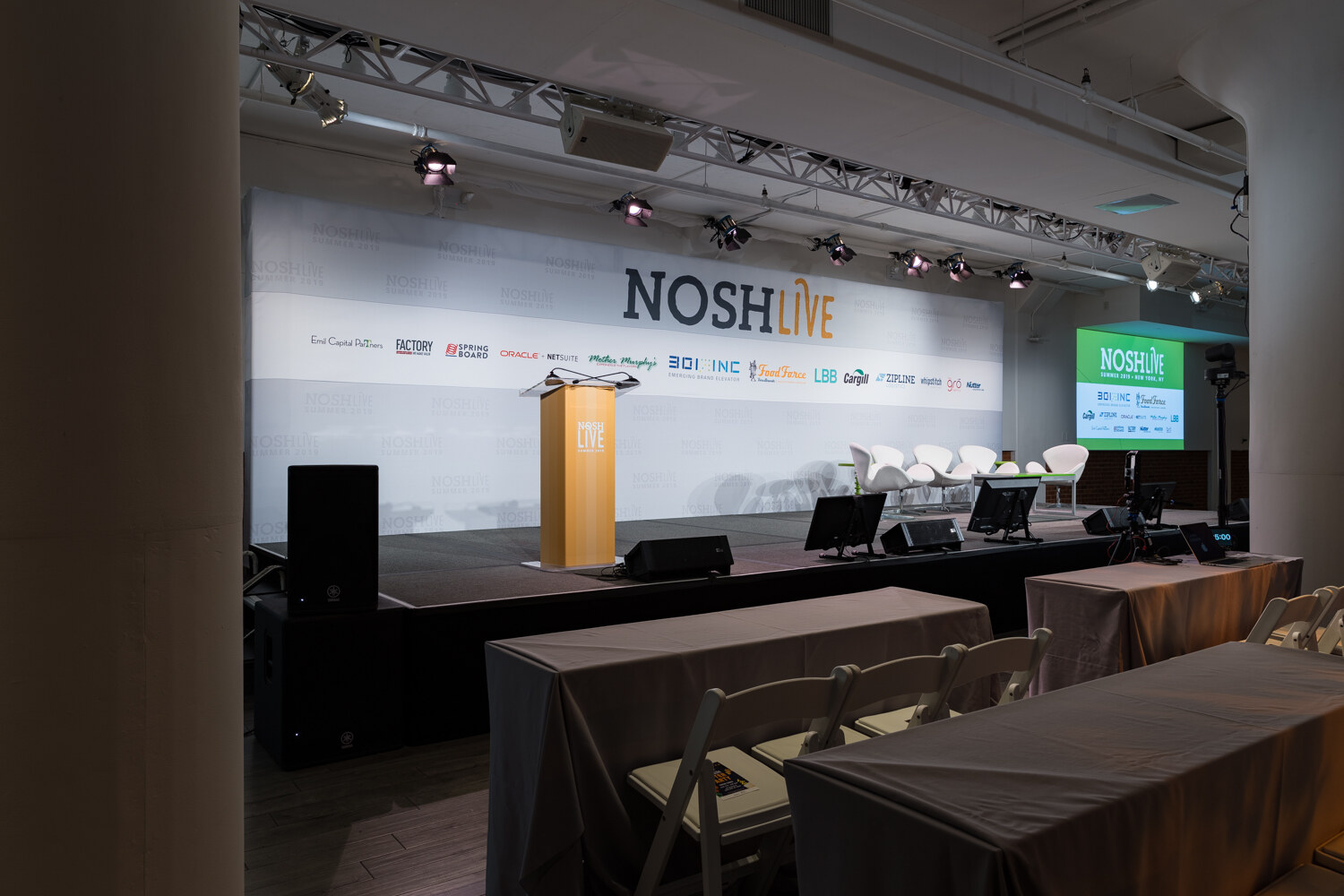 Wide view of the stage, lectern and green video screens before the session