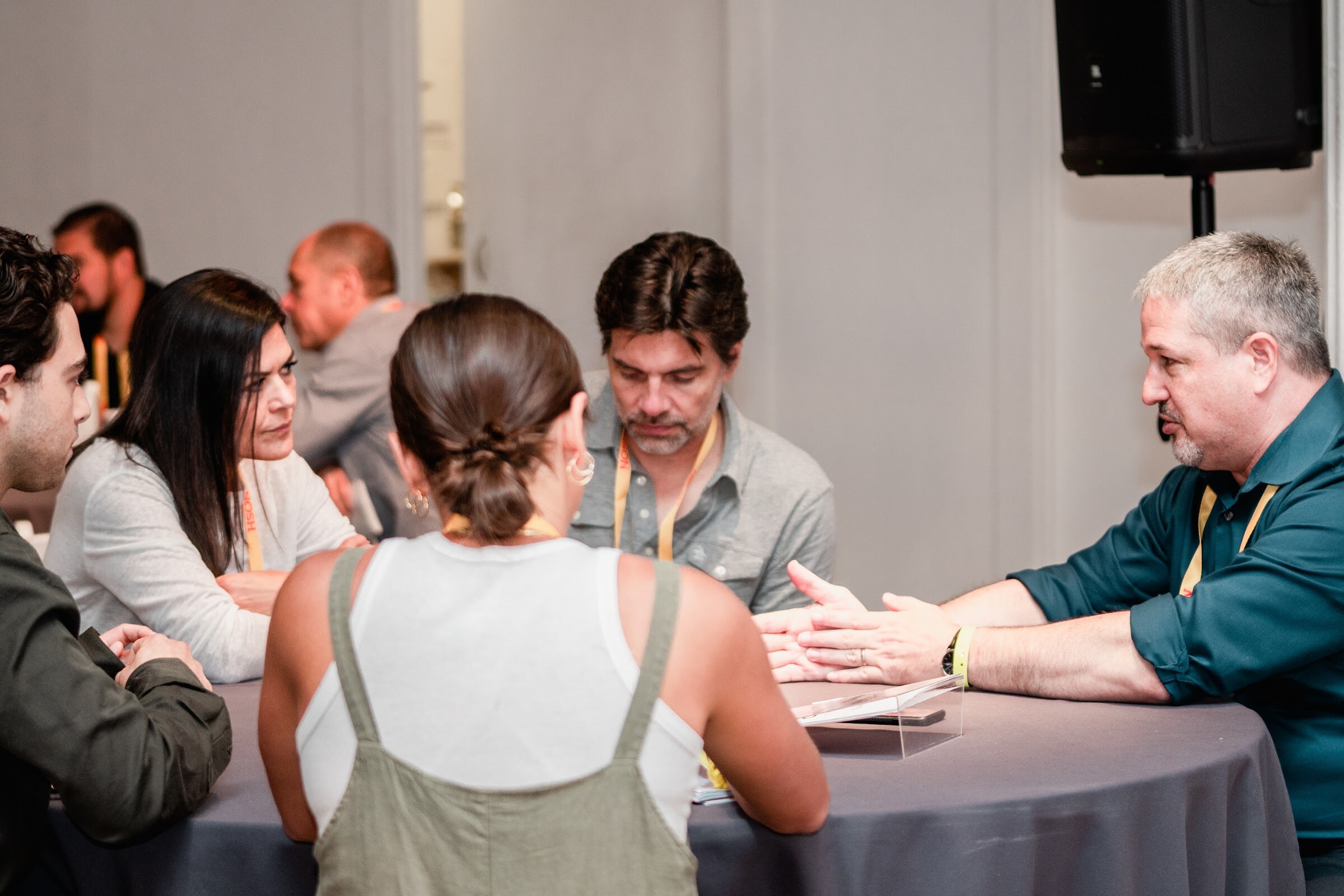 Two men in glasses and gray shirts talking with two women around a round table with a gray cloth.