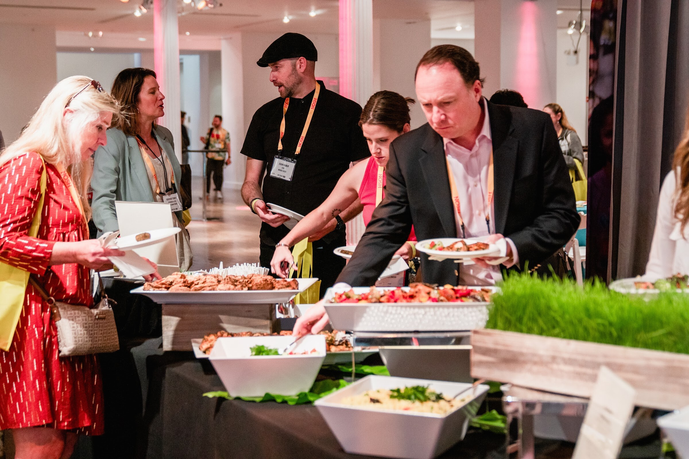 Group serving themselves from white bowls and trays on a black buffet table with a tray of wheatgrass.