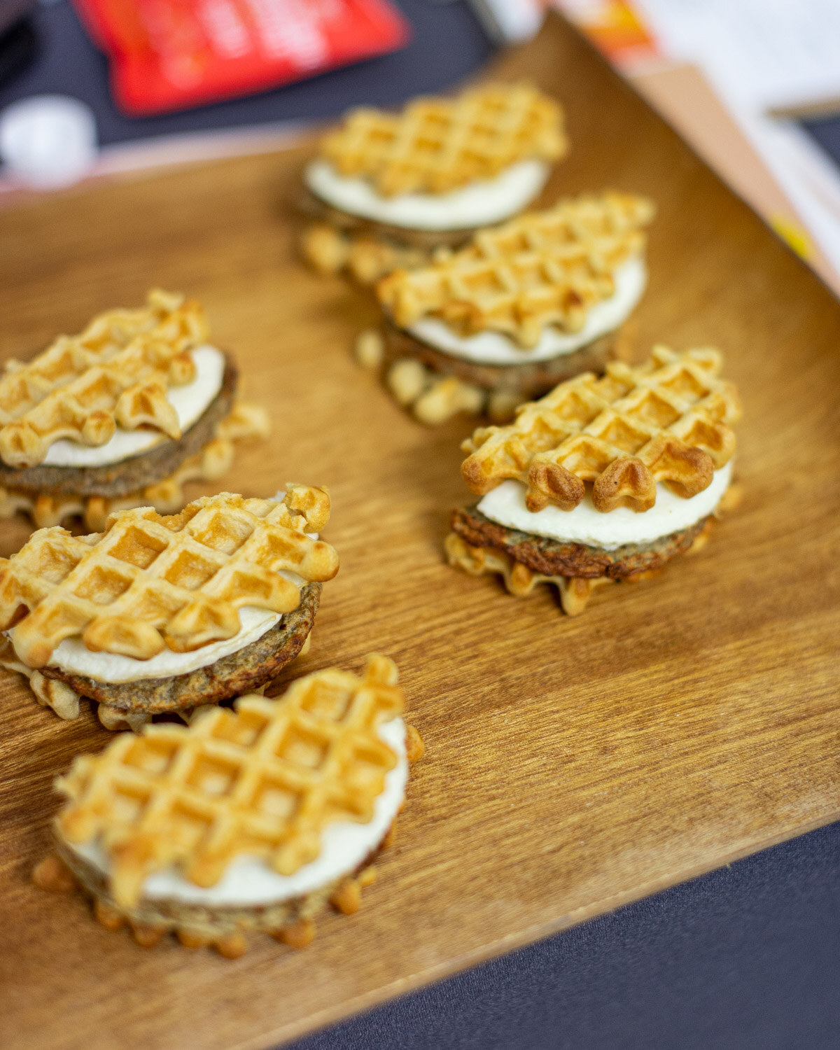 Overhead view of five mini waffle sandwiches with cream filling on a wooden serving board.
