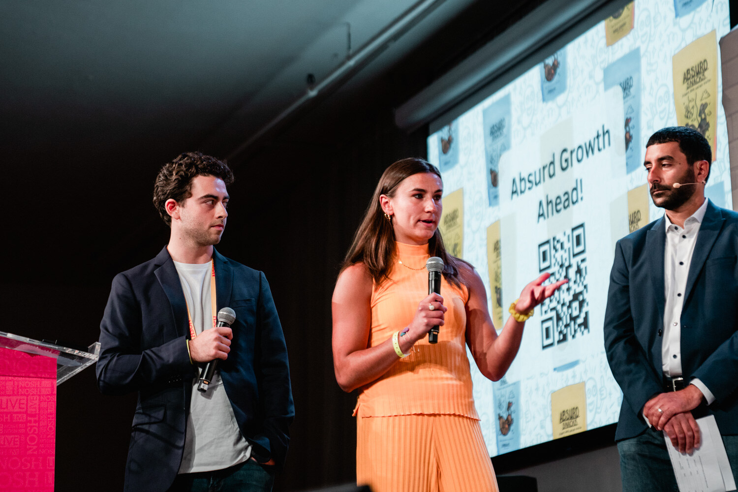 Three people standing on stage in front of a slide that reads Absurd Growth Ahead with a QR code.