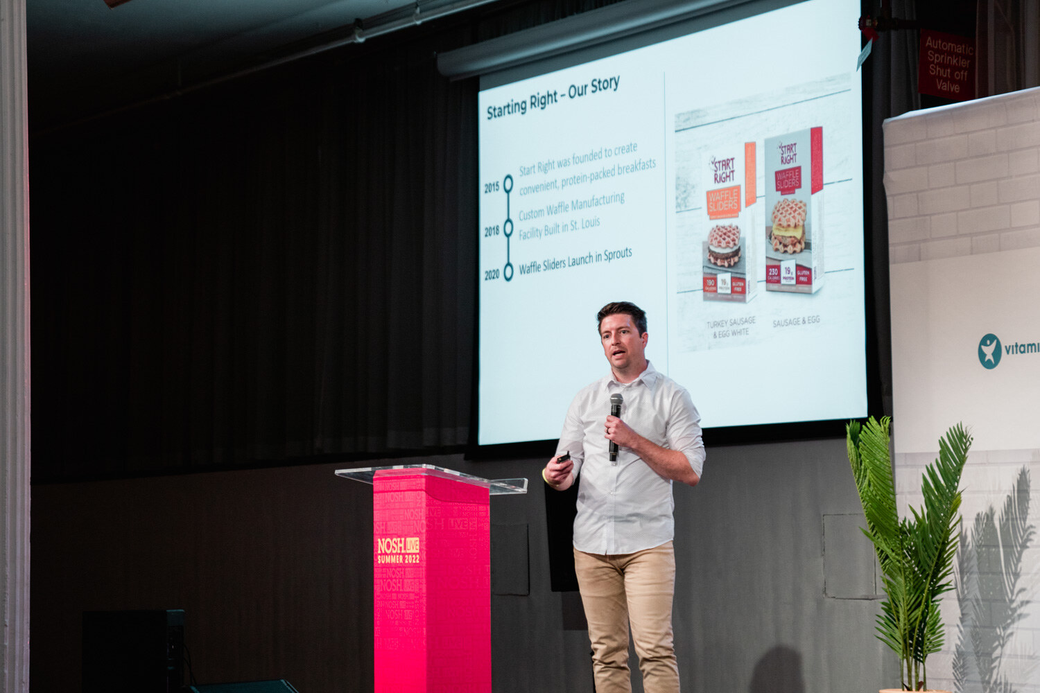 Man in a light shirt and khakis with a mic beside a red podium in front of a slide titled Starting Right Our Story.