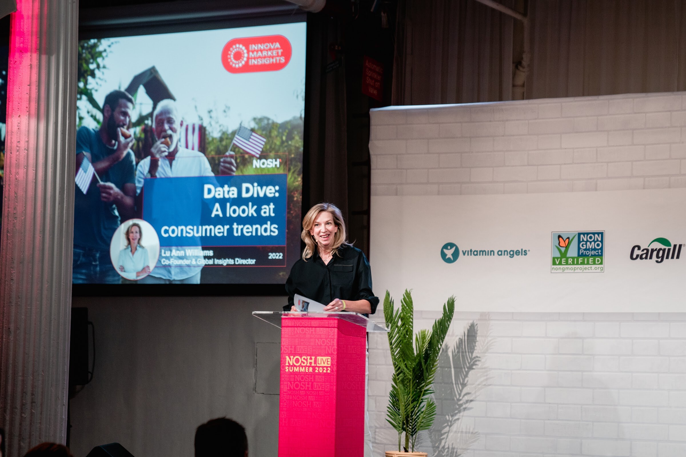 Woman at a red podium beside a screen titled Data Dive: A look at consumer trends.