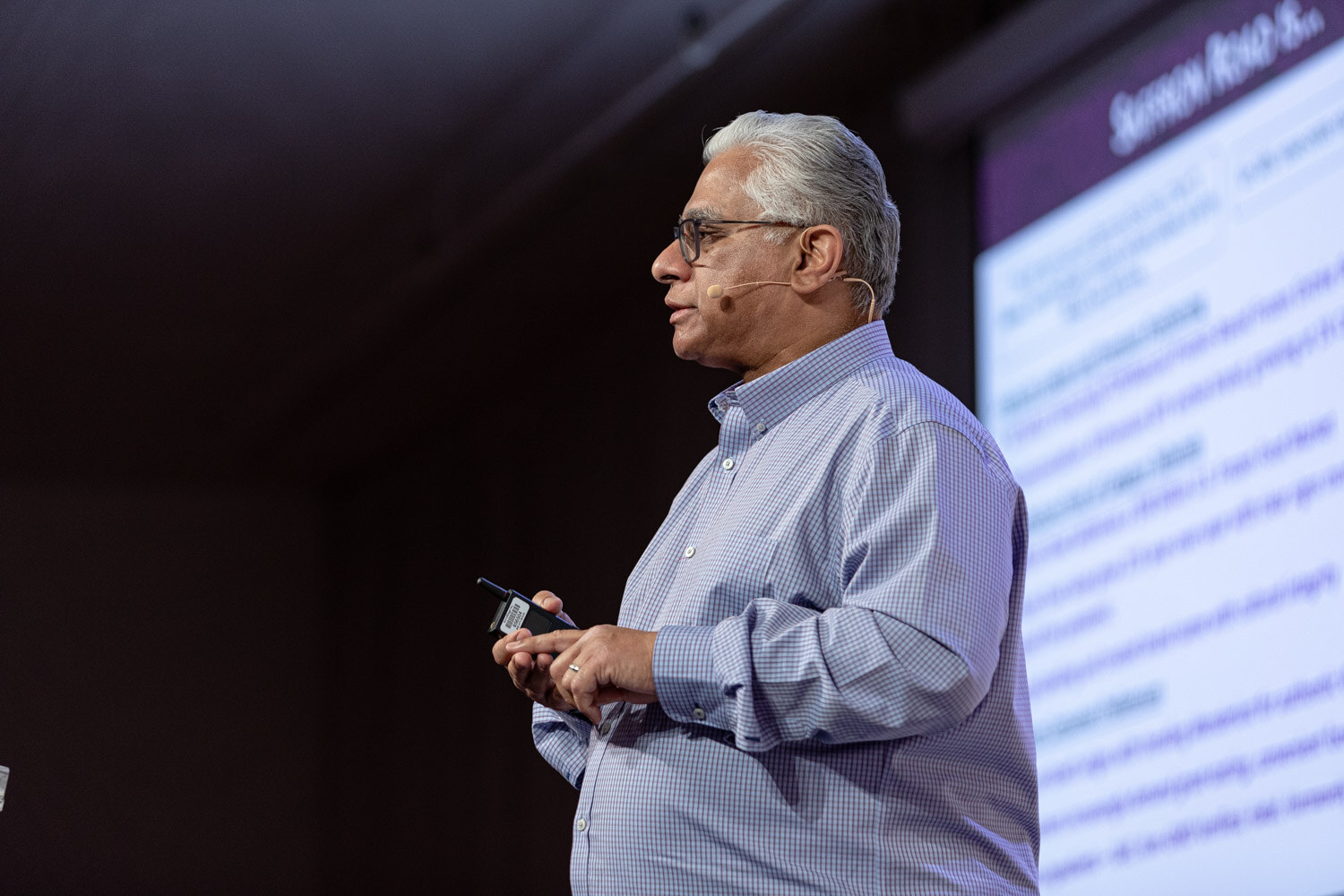 Gray-haired man in glasses and a blue shirt standing in profile beside a purple slide.