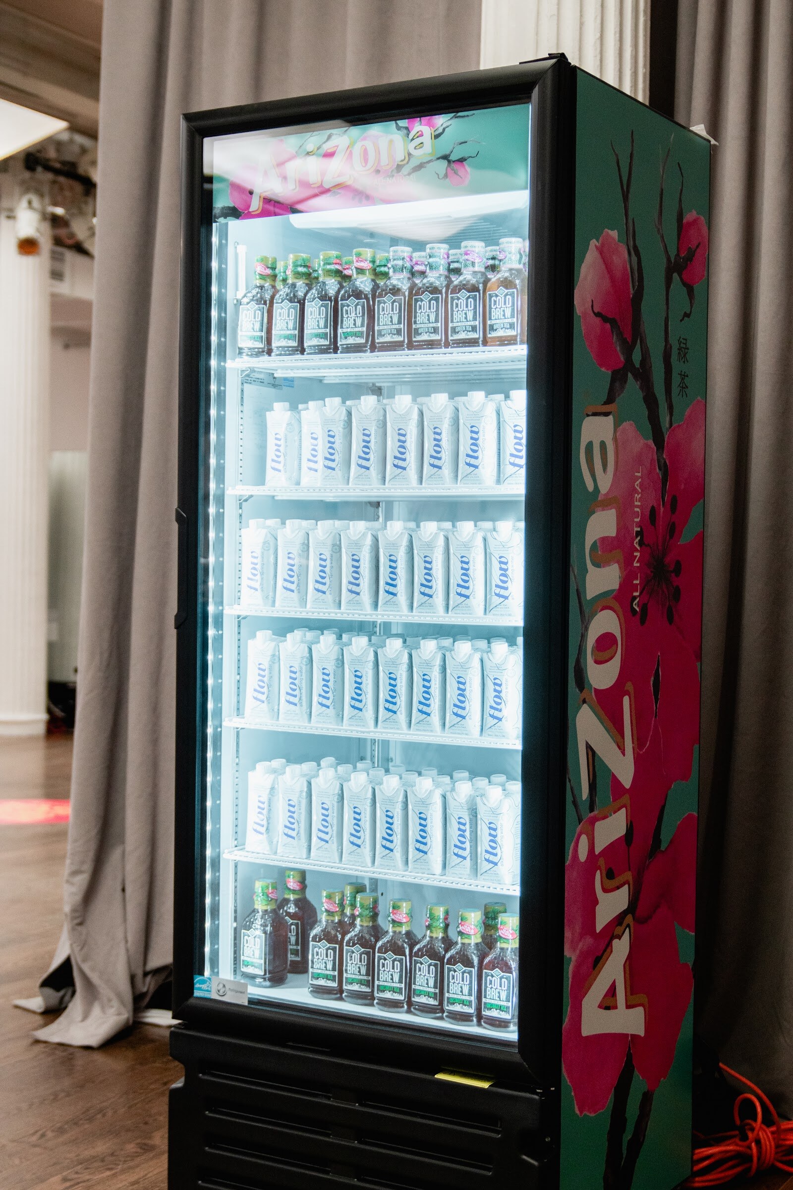 Glass-door cooler with a pink floral Arizona design and rows of bottles lit from inside.