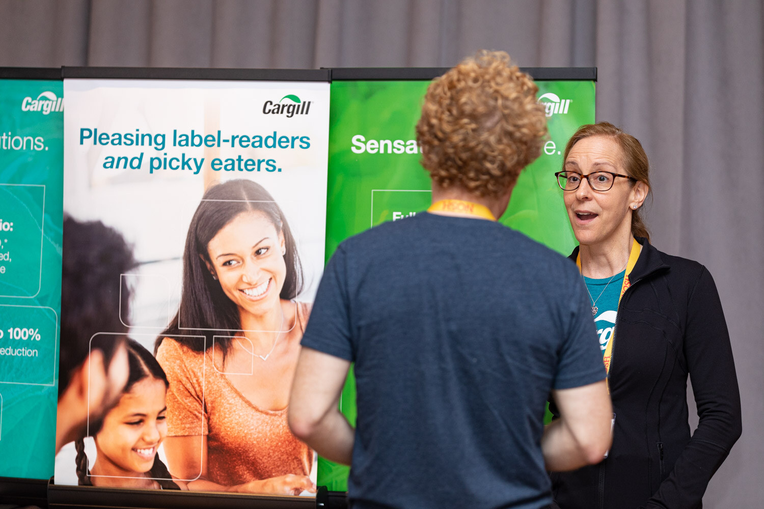 Man with curly hair and woman in glasses and a black jacket in front of a Cargill banner reading Pleasing label-readers and picky eaters.