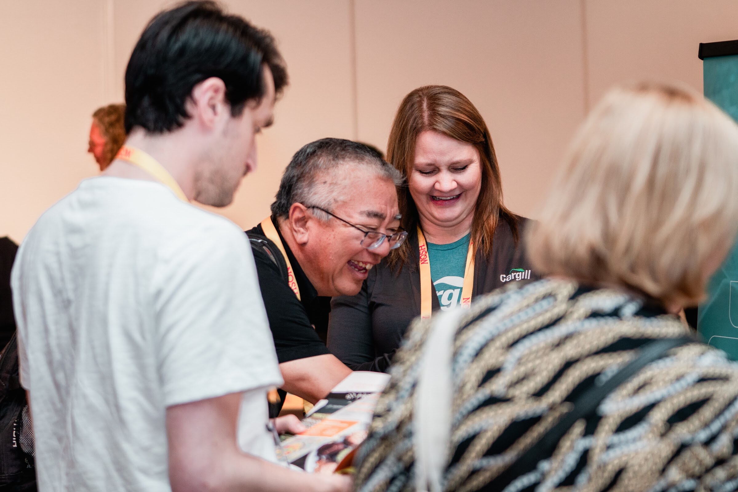 Group leaning over a table, a woman in a Cargill shirt laughing with a man in glasses beside her.