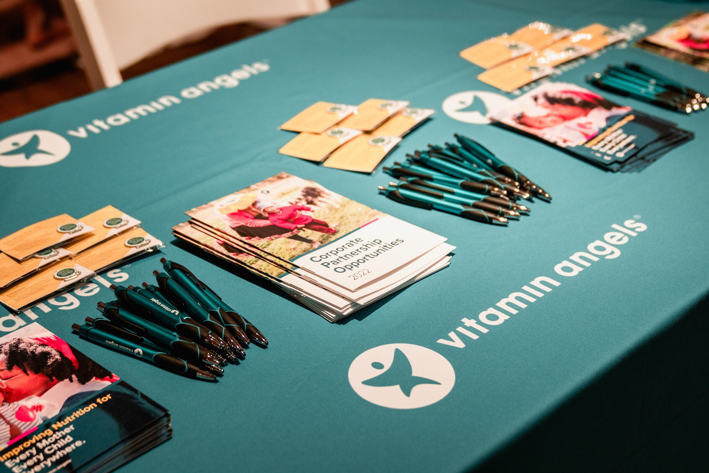 Teal tablecloth printed with the Vitamin Angels logo, covered with brochures and pens.