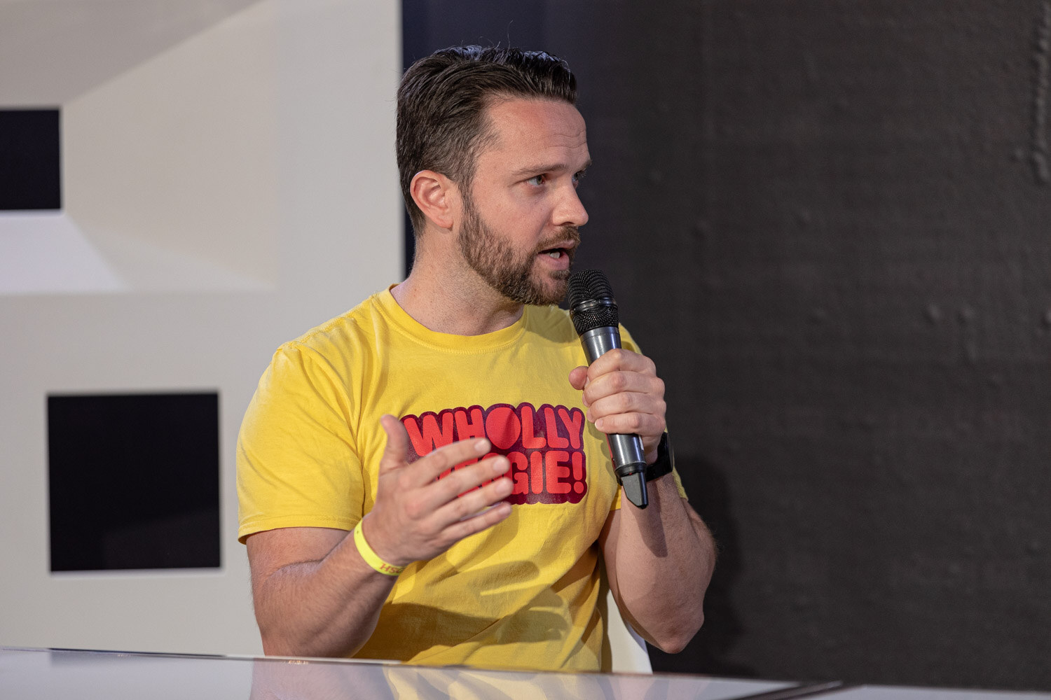 Bearded man in a yellow Wholly Veggie t-shirt speaking into a mic.