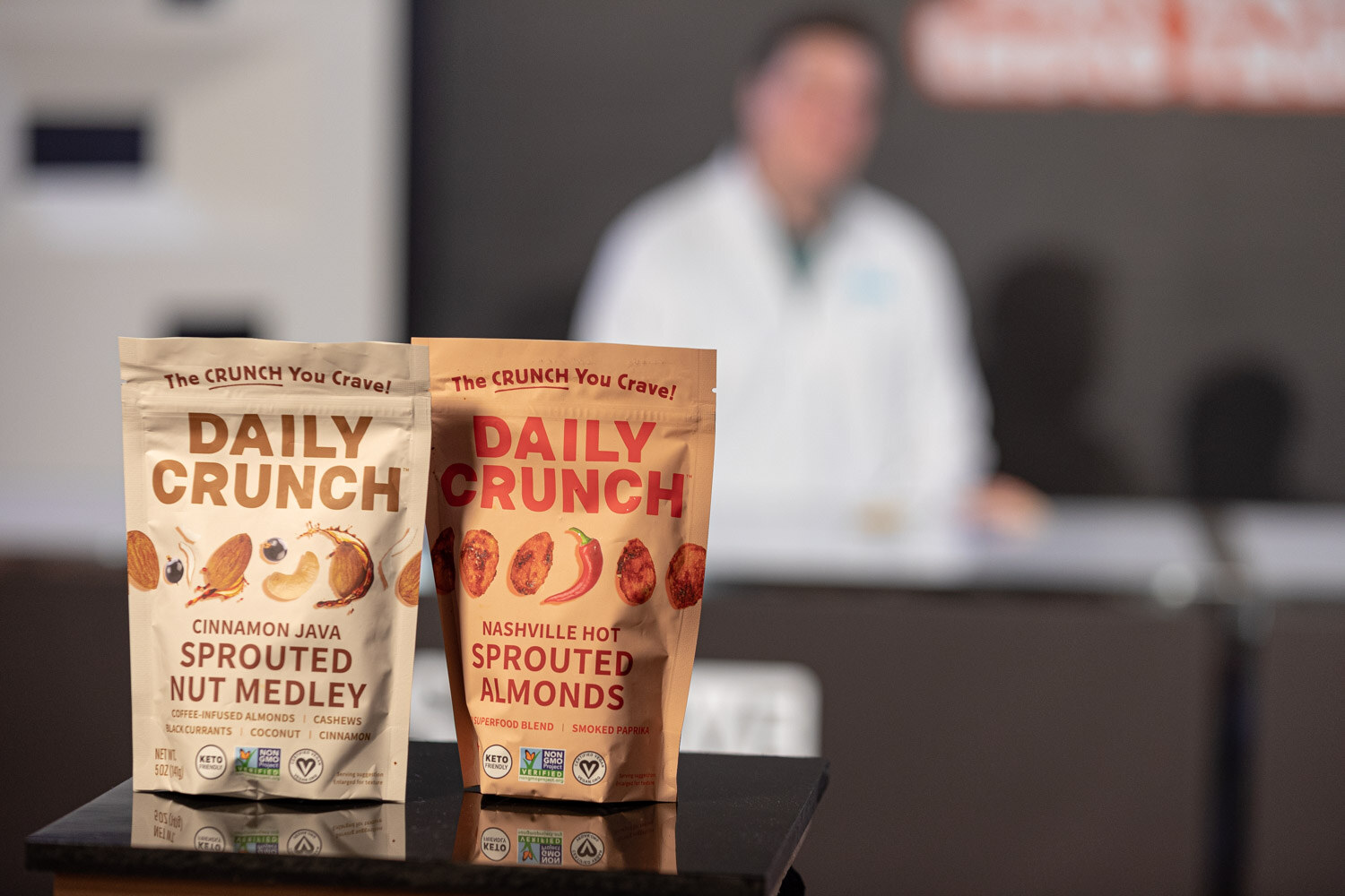 Two tan pouches labeled Daily Crunch in front of a blurred person in white.
