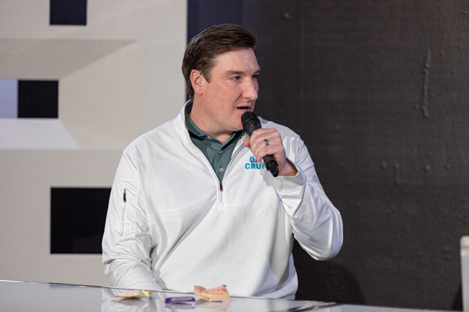 Man in a white quarter-zip pullover with a Daily Crunch logo speaking into a mic.