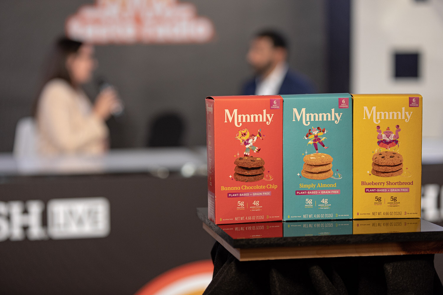 Red, teal and yellow Mmmly boxes in front of a blurred interview.