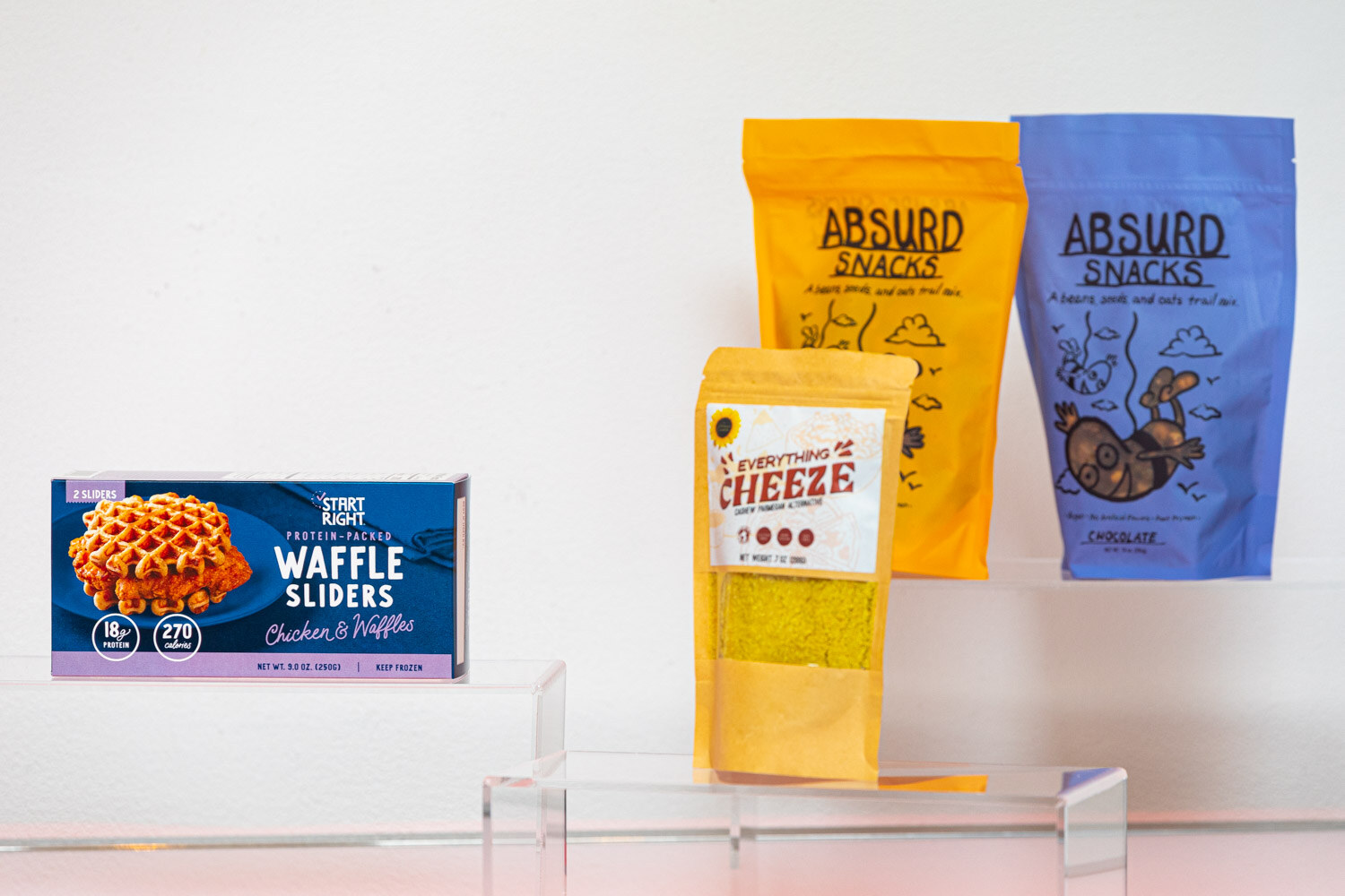 Start Right Waffle Sliders box, yellow Everything Cheeze pouch and two Absurd Snacks pouches on acrylic stands.