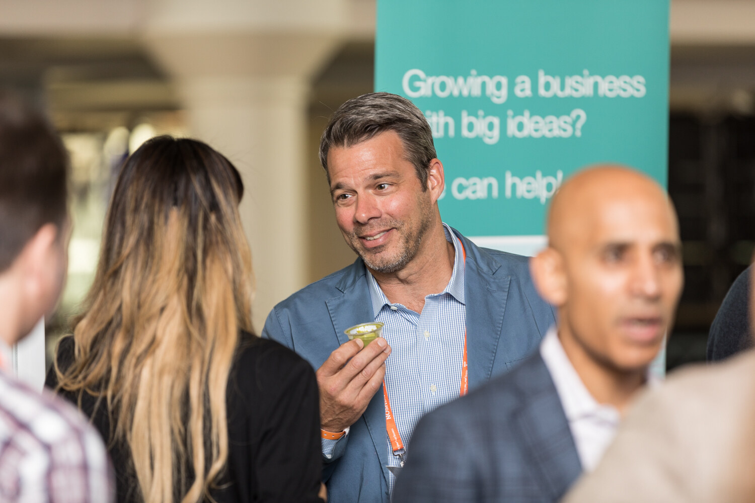 A smiling man in a blue blazer holds a small cup of green sample in front of a teal banner reading Growing a business with big ideas.