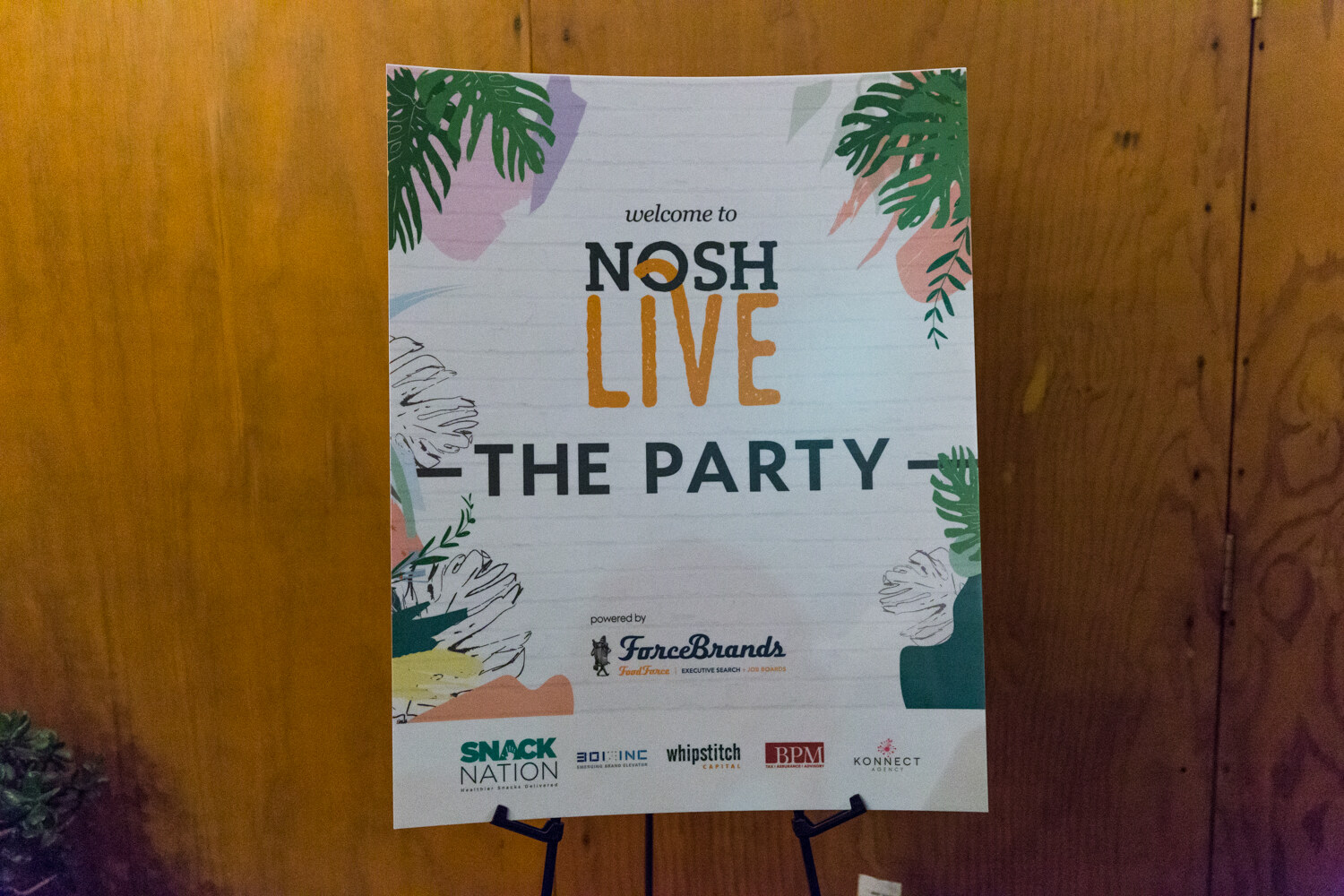 A poster with tropical leaf artwork reads welcome to NOSH Live, The Party, powered by ForceBrands, with Snack Nation, 301 Inc, Whipstitch Capital, BPM and Konnect Agency logos below.
