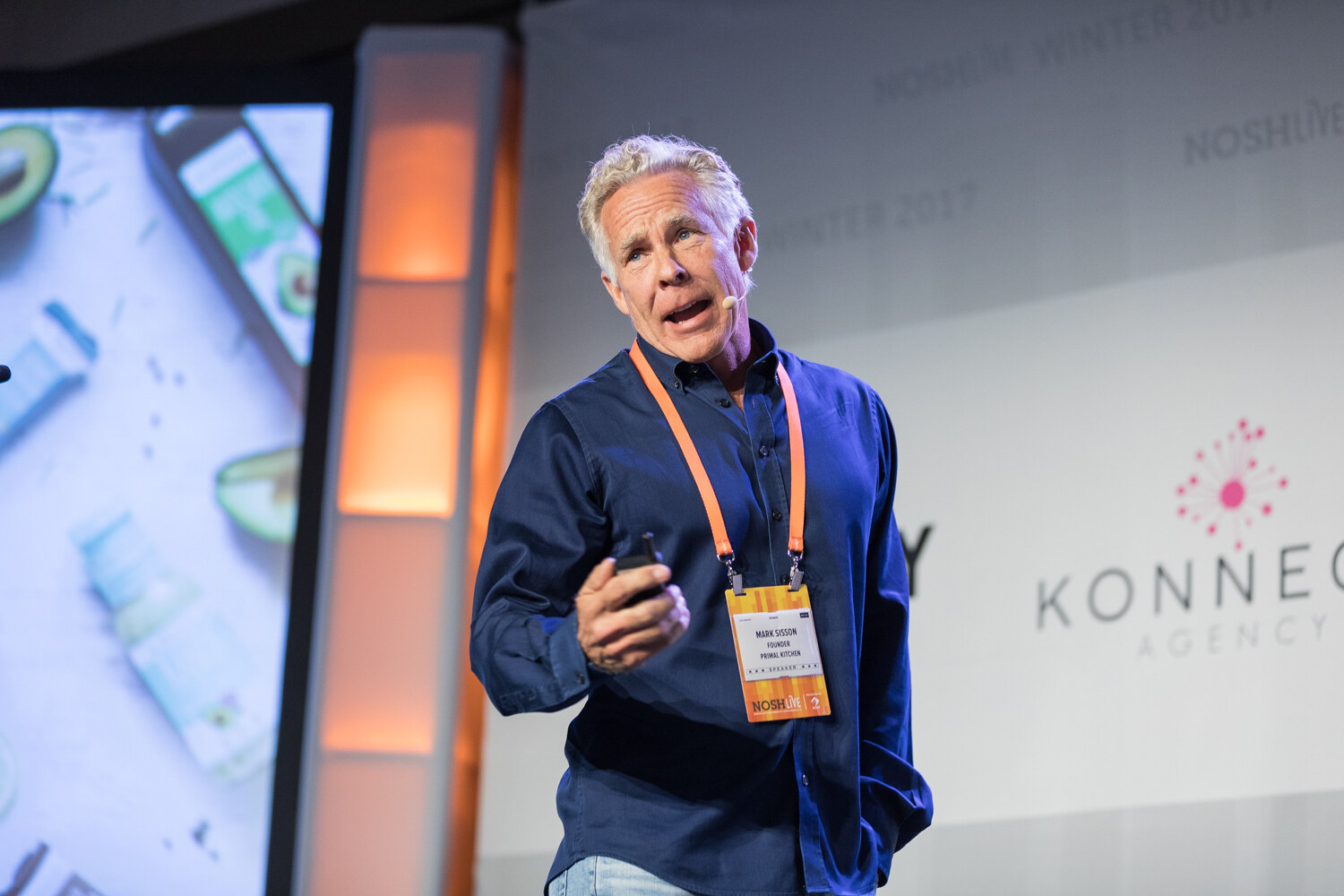 A gray-haired man in a navy shirt with an orange lanyard speaks on stage, with a slide of avocado and packaged products at left and a Konnect banner at right.
