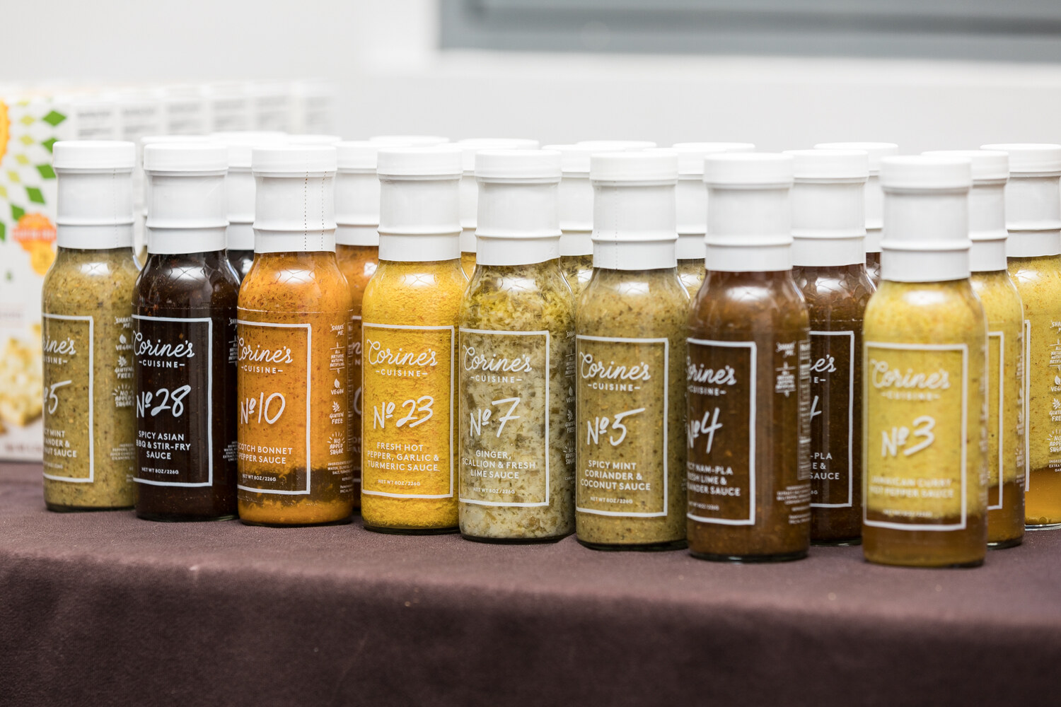 Two rows of sauce bottles with white caps labeled Corine's Cuisine and numbers such as No 28, No 10, No 23 and No 5, in shades of brown, orange and yellow.