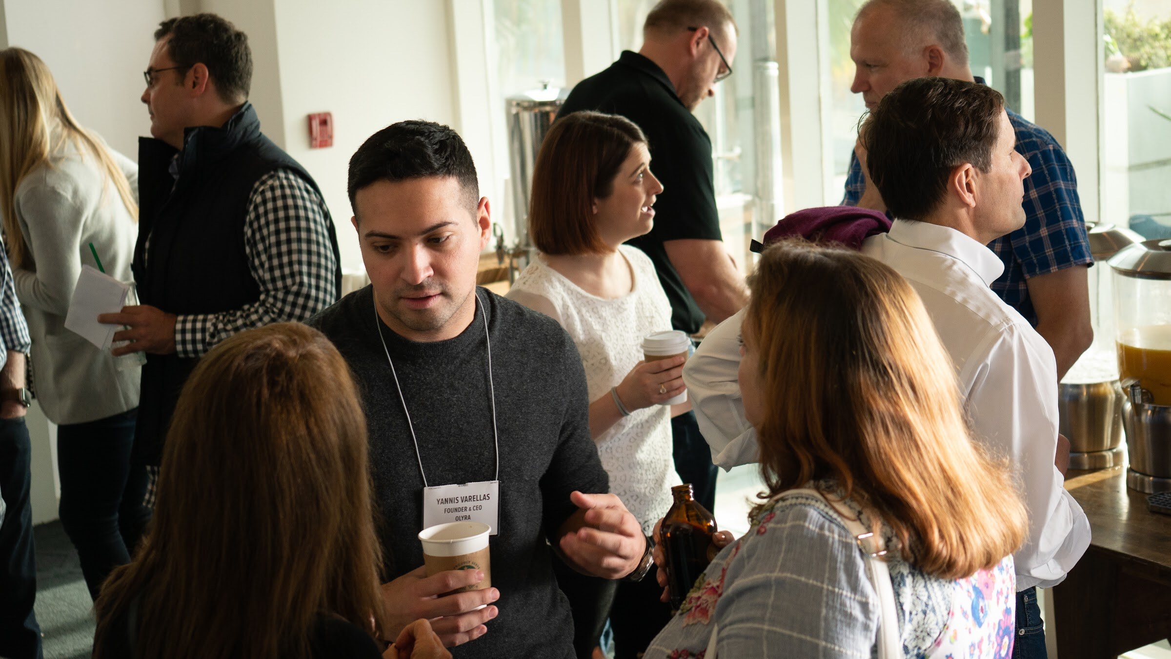 Attendees network over coffee in a sunlit room.