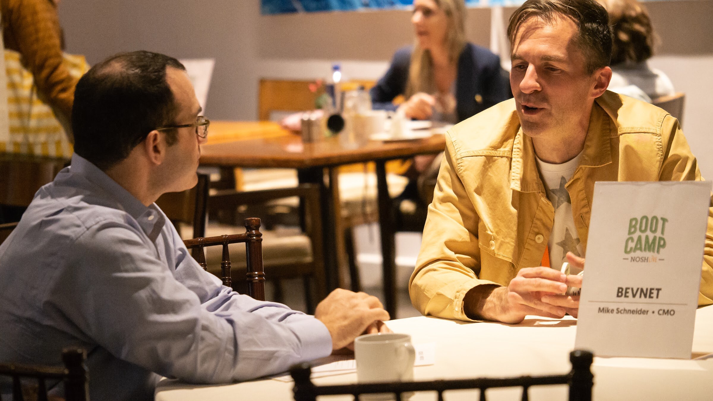 Two men talk at an expert table marked with a BevNET table card.