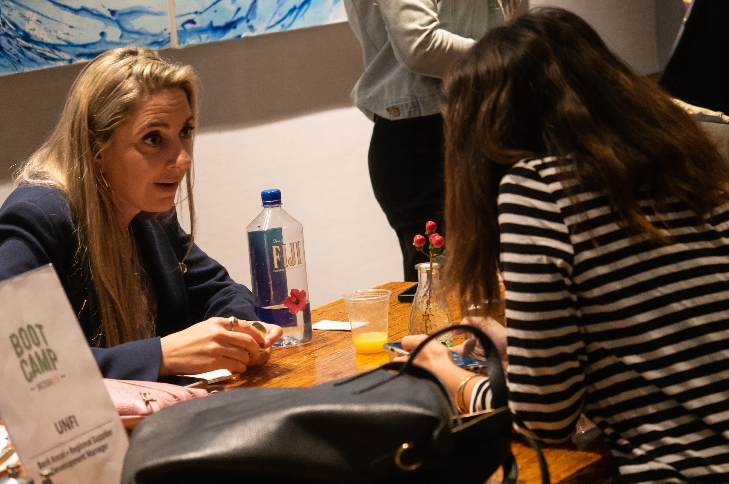 A woman in a navy blazer talks with attendees at a Boot Camp expert table.