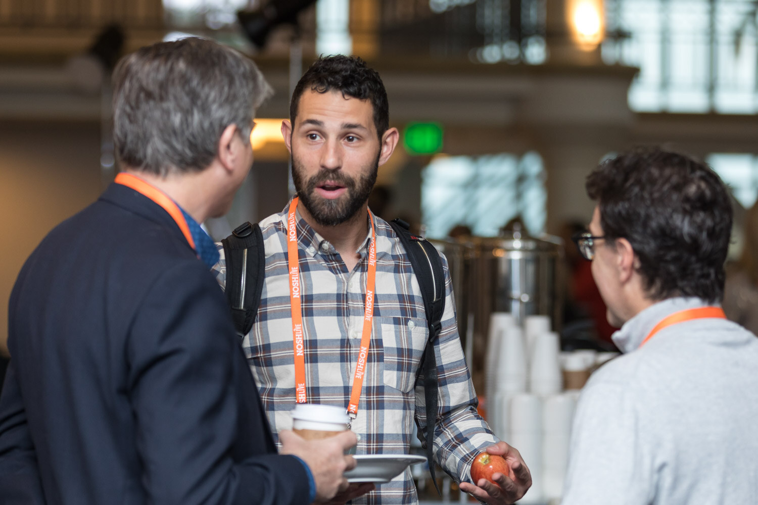 Two men in lanyards talk over coffee during the morning break.