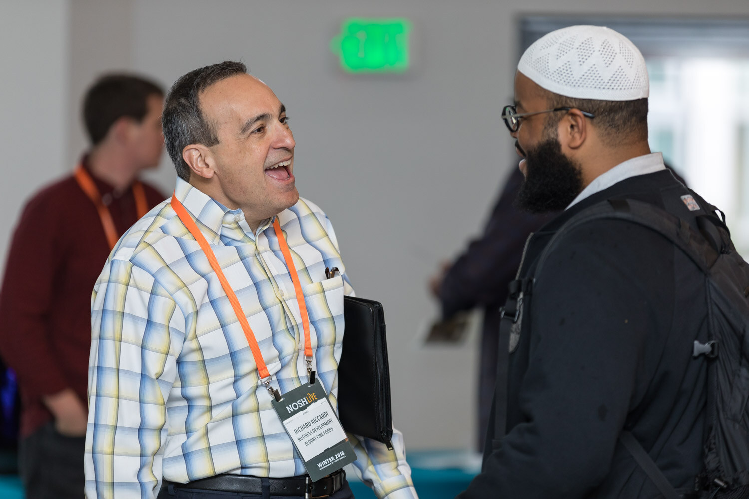A man in a plaid shirt laughs while talking with another attendee.