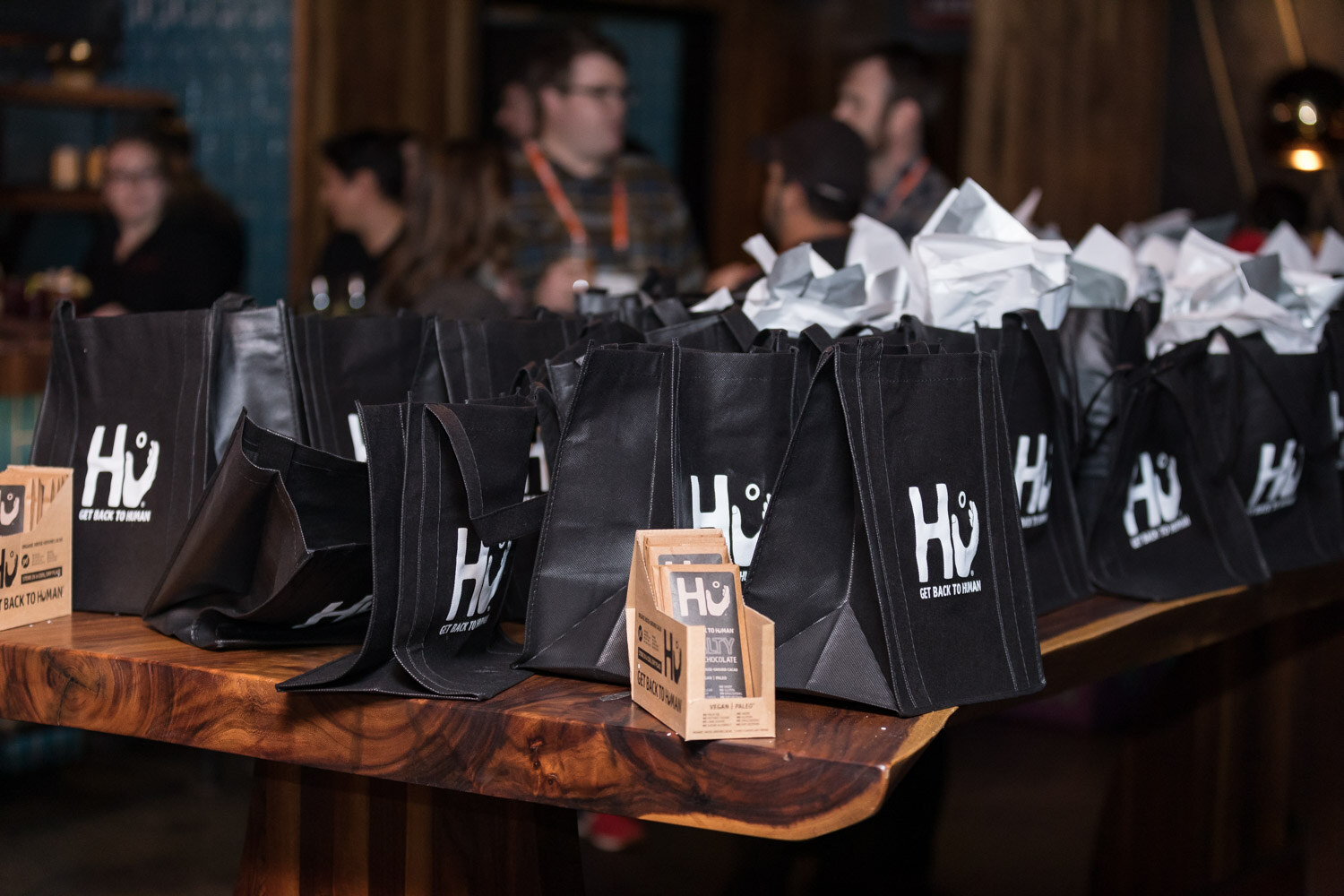 Black Hu tote bags lined up on a wooden bar at the afterparty.