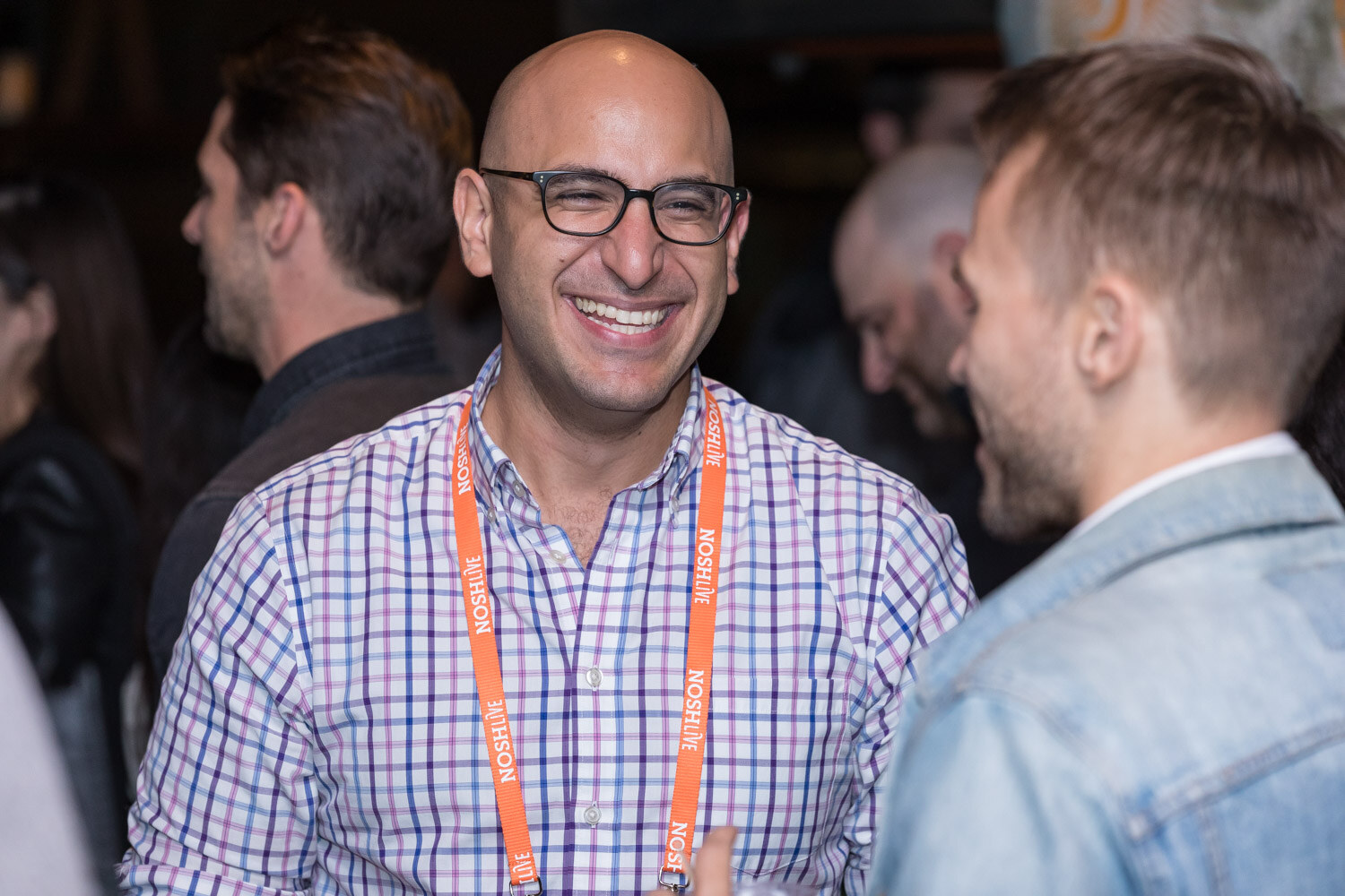 A smiling man in a plaid shirt and orange lanyard at the afterparty.