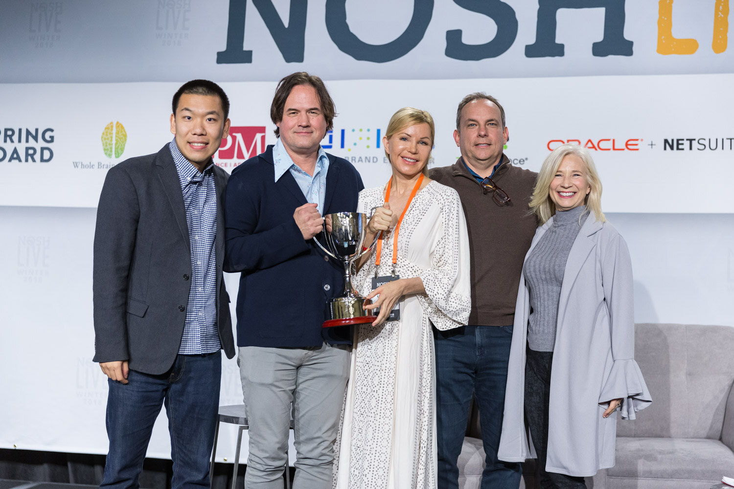 Five people pose on stage with the Pitch Slam trophy in front of the Nosh Live sponsor wall.