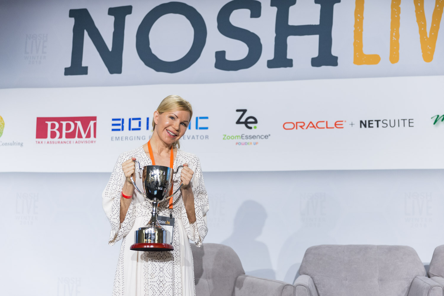 A woman in a white dress holds up the Pitch Slam trophy on stage.