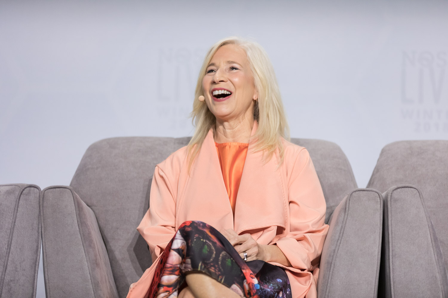 A woman in a peach jacket laughs during an on-stage interview.