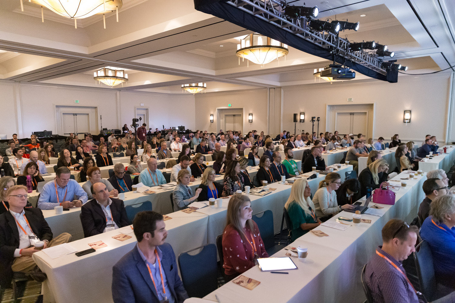 A wide view of attendees seated at long tables facing the stage in the main ballroom.