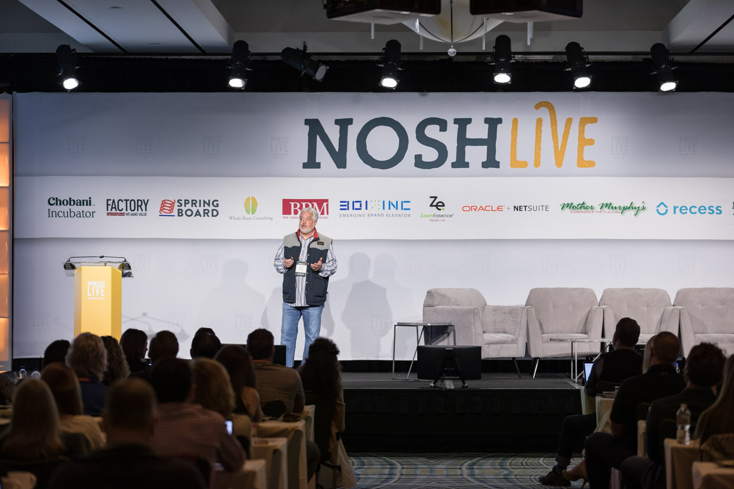 A presenter stands on the main stage in front of a seated audience under the Nosh Live banner.