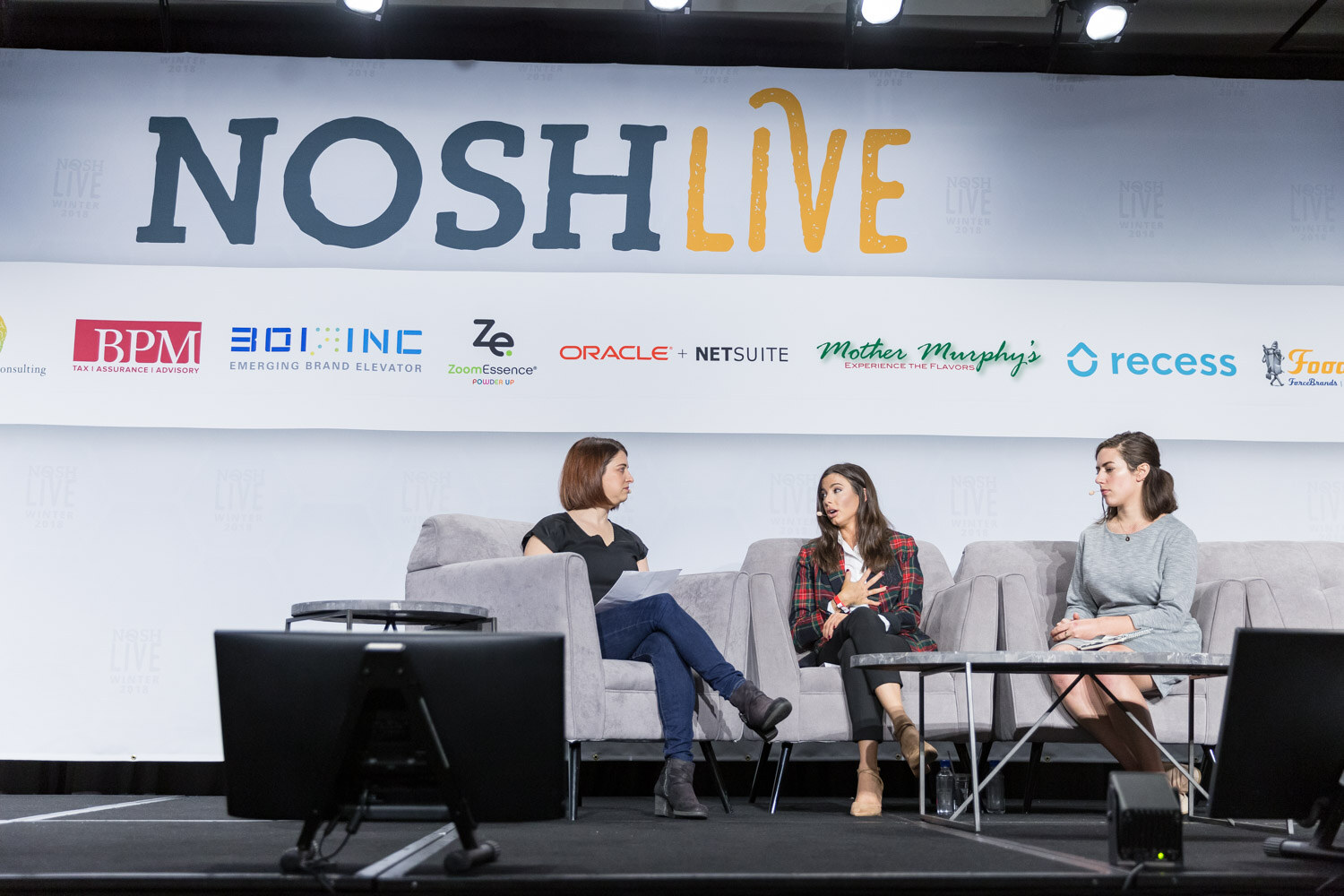 Three women sit in gray armchairs on the main stage under the Nosh Live banner.