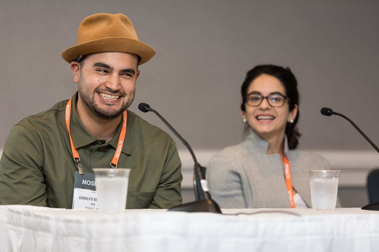 Two panelists, one in a tan hat, smile at the head table during Breakout Session 2.