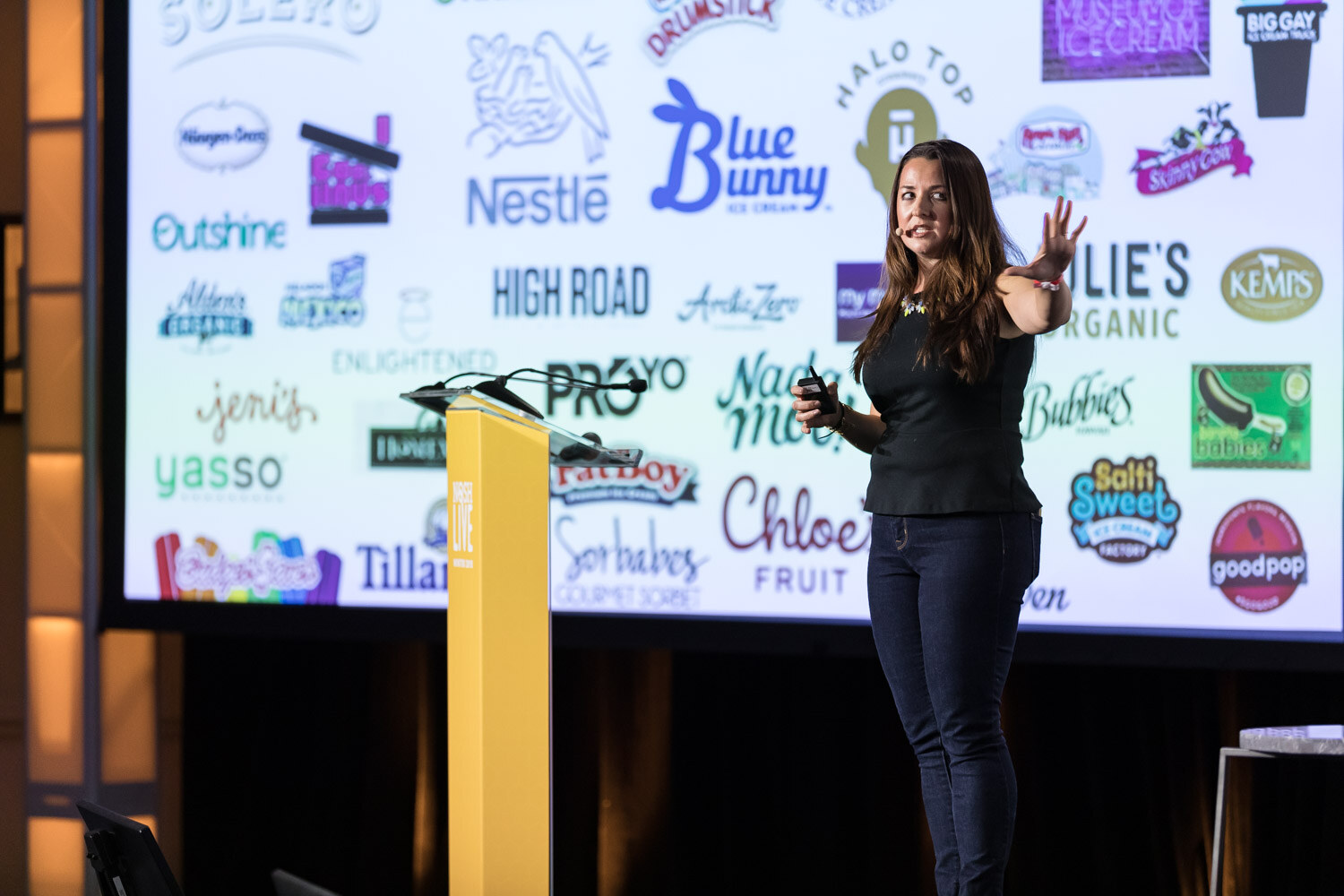 A presenter stands beside the lectern in front of a slide of ice cream and frozen food brand logos.